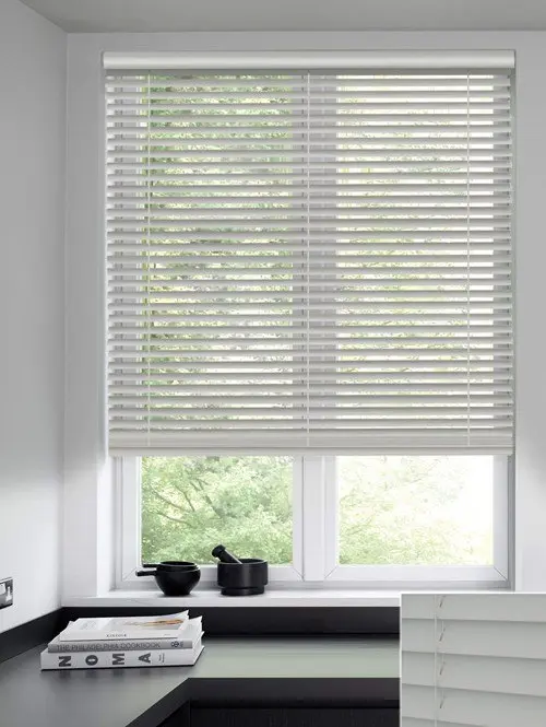 White venetian blinds with the slats tilted, fitted above a kitchen worktop